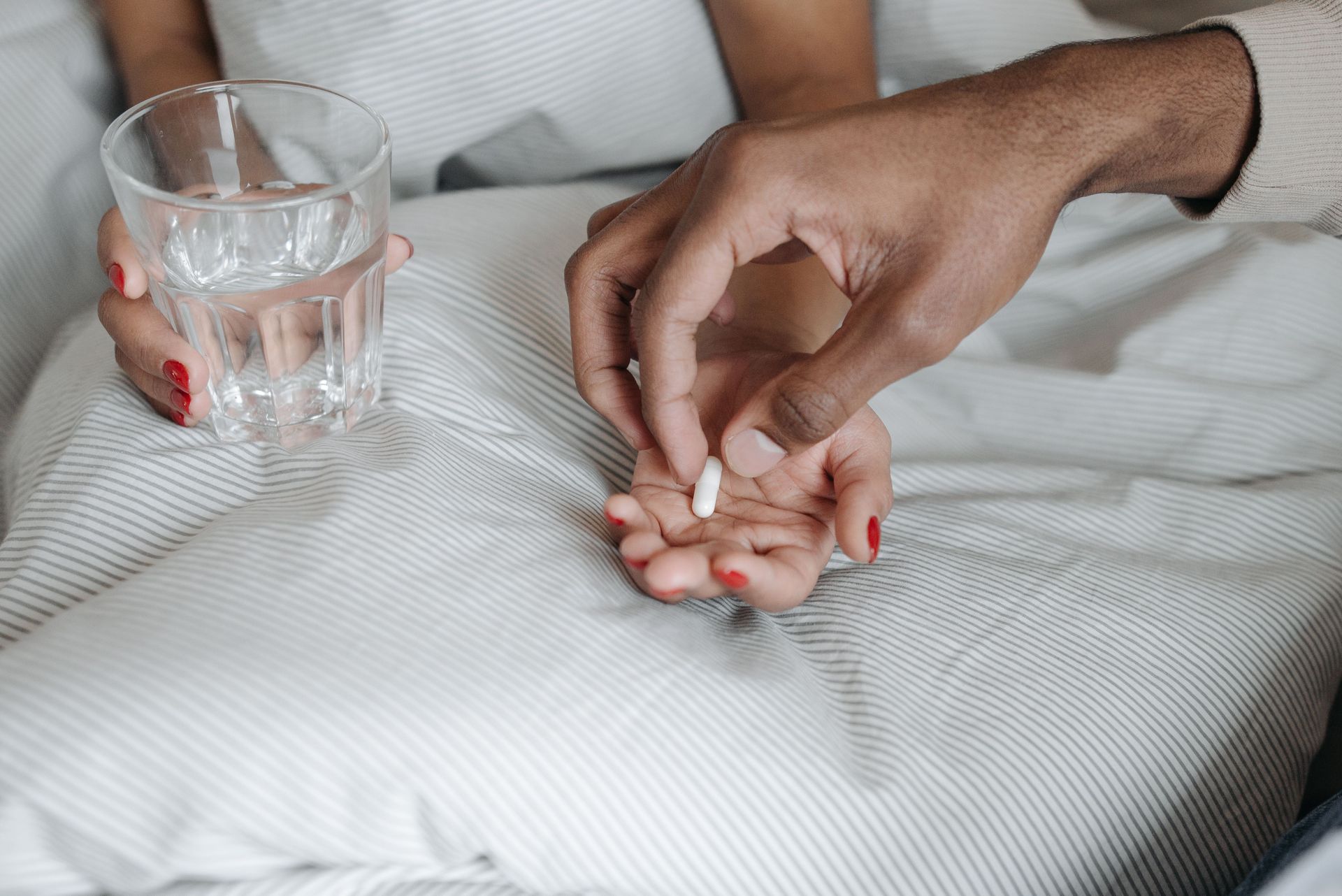 Close-up of hands offering a pill with a glass of water, symbolizing care and medication.